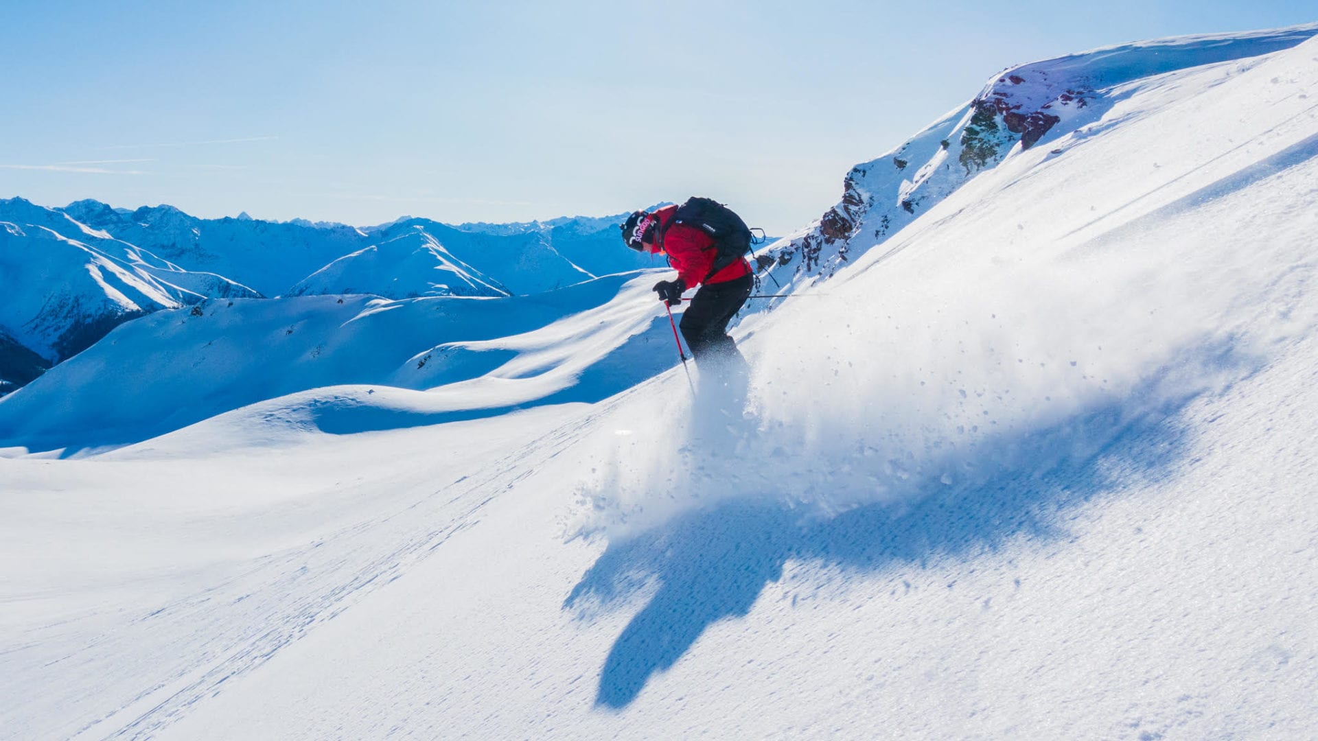 man wearing a red jacket skiing down in off piste