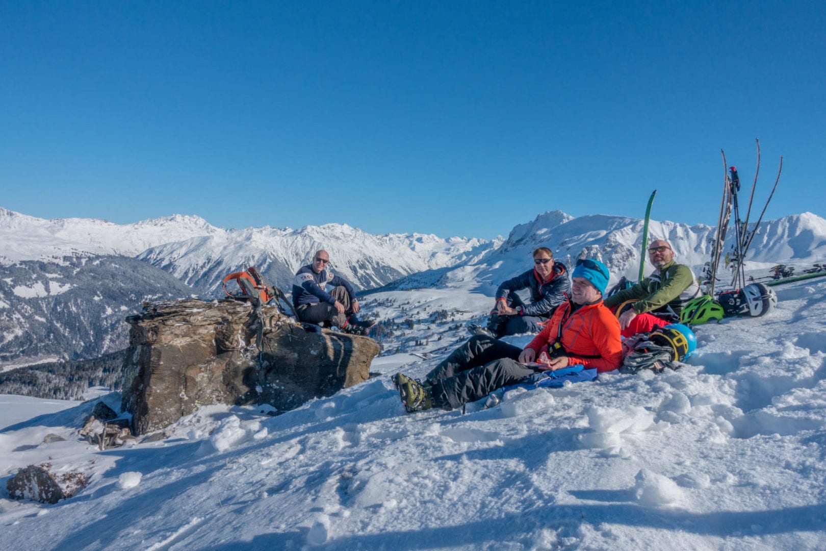 four skiers sitting on the snow with ski equipments